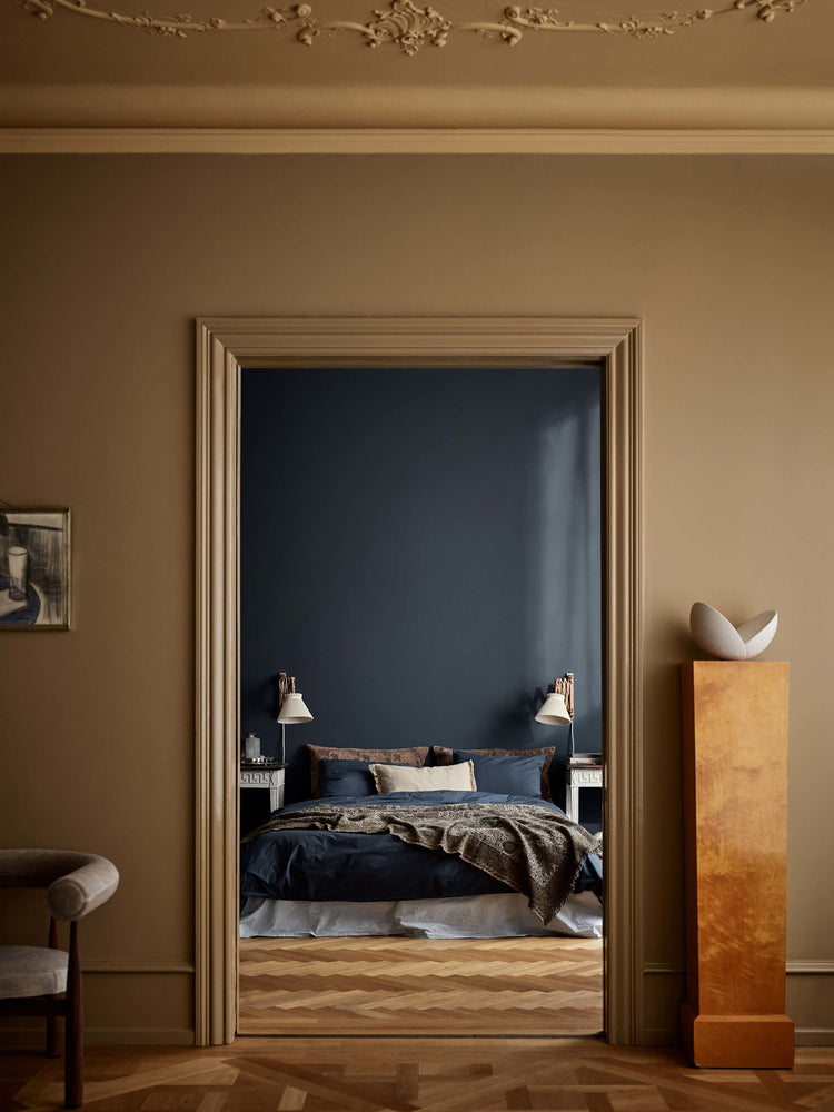 En stue med vægge i brun Jotun 1799 Spice Brown og loft i okkergul Jotun 1909 Kalkoker, med udsigt ind til et soveværelse med en dyb blå væg malet i Jotun 4403 Midnight Blue.