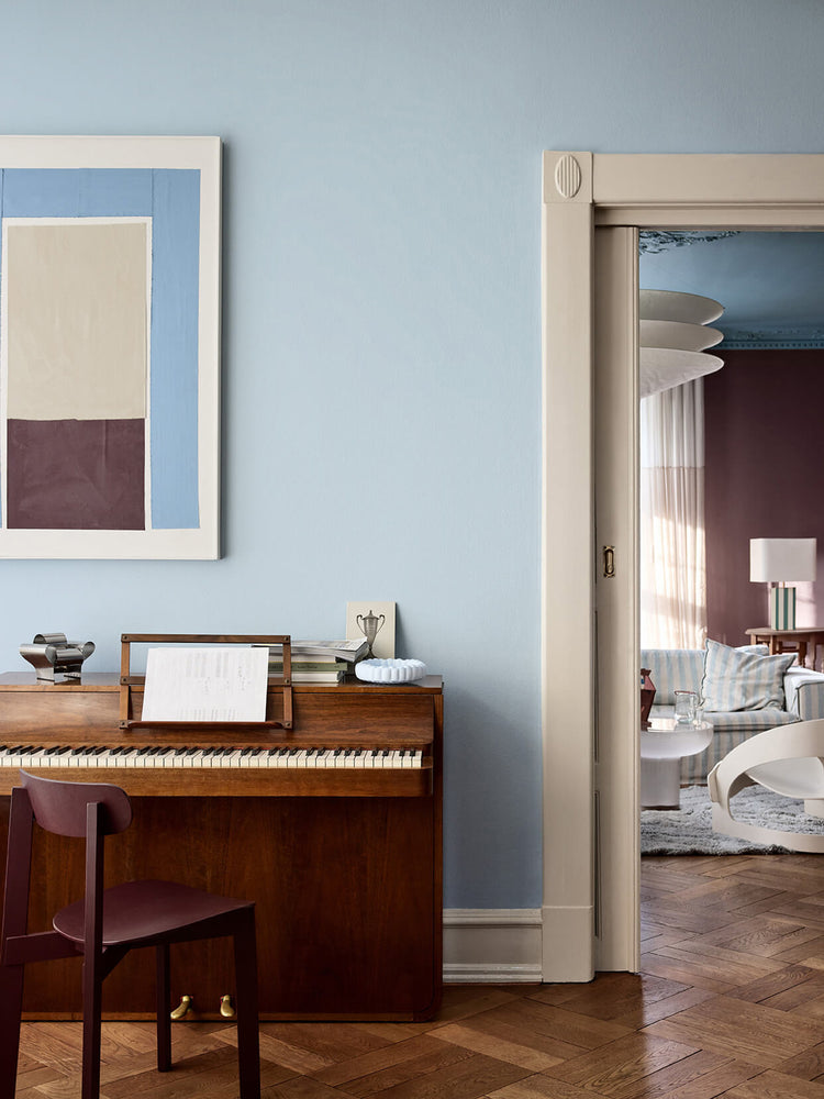 En stue med vægge i den lyseblå farve Jotun 40054 North, listværk i den beige nuance Jotun 12299 Beige Sheen og den brunlilla Jotun 3343 Dusty Purple i baggrunden. Rummet er indrettet med et klaver i træ og en stol.
