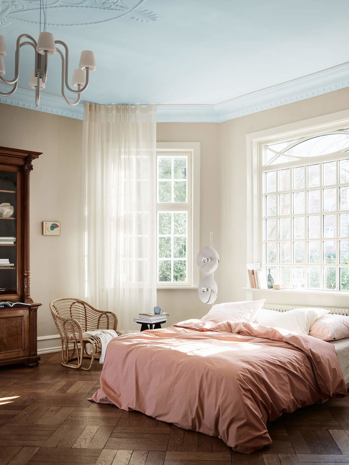Et luftigt soveværelse med beige vægge malet i Jotun 12299 Beige Sheen, et loft malet i den lyseblå nuance Jotun 40054 North, hvide vindueskarme i Jotun 11364 Century White samt en rosa dyne.