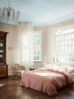 Et luftigt soveværelse med beige vægge malet i Jotun 12299 Beige Sheen, et loft malet i den lyseblå nuance Jotun 40054 North, hvide vindueskarme i Jotun 11364 Century White samt en rosa dyne.