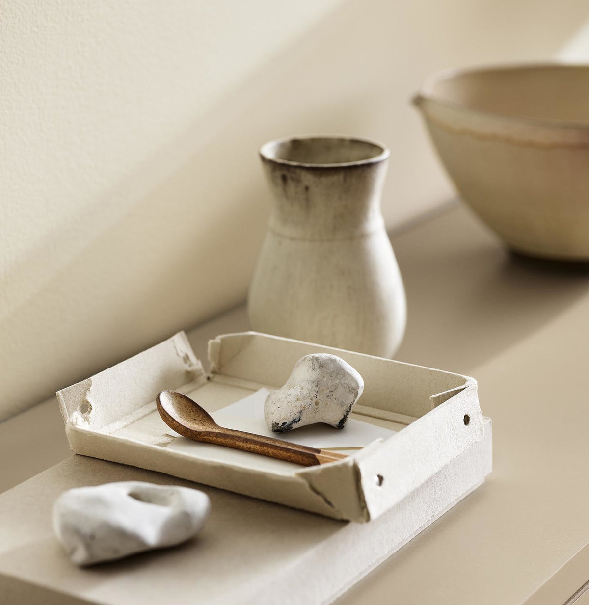 A ceramic vase, tray, and white stones against a wall painted with the colour 1625 Soul from Jotun.