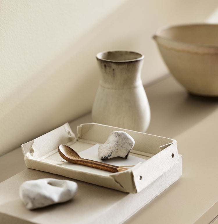 A ceramic vase, tray, and white stones against a wall painted with the colour 1625 Soul from Jotun.