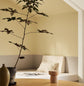 A potted plant and a daybed with light bedding against muted, greenish yellow walls painted in the colour 1965 Ginger Tea from Jotun.