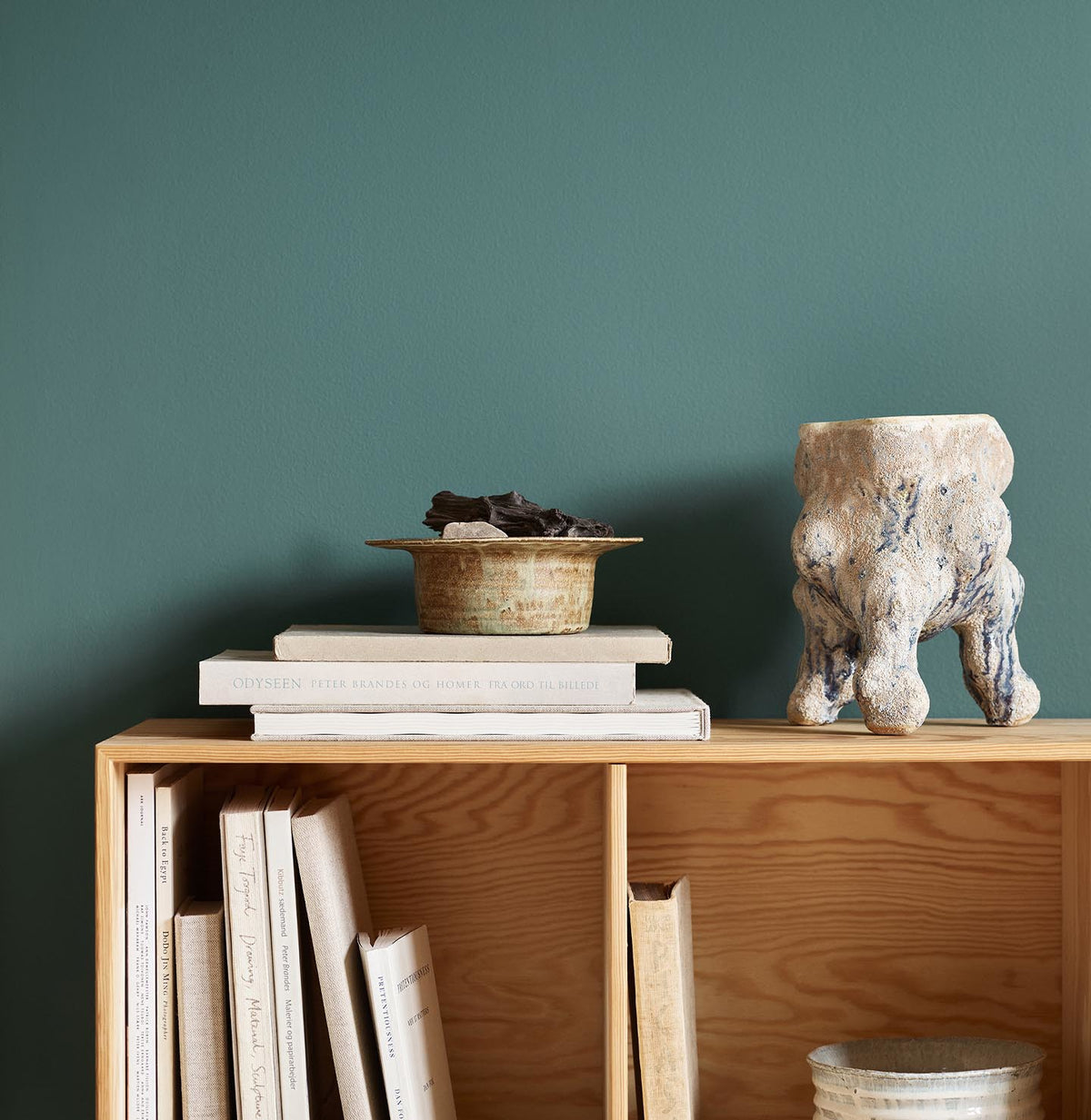 Bookshelf with stacked books, bowl, and ceramic sculpture against a green wall painted in the Jotun colour 6194 Wild Ivy.
